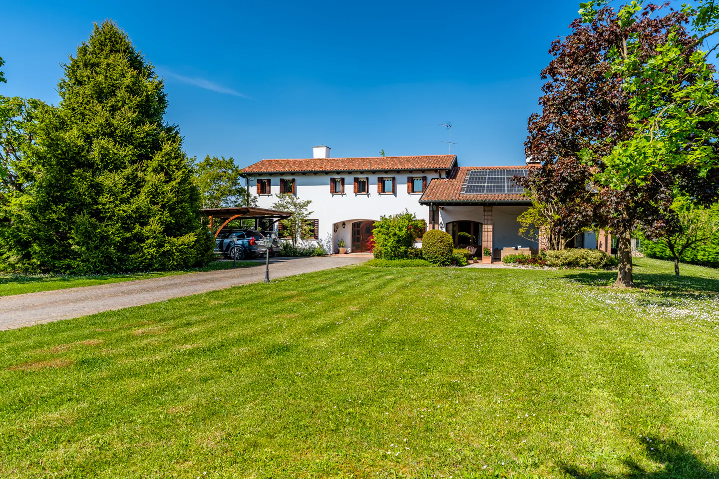 Exterior view of a white house with a red tile roof, green lawn, and a car under a carport.