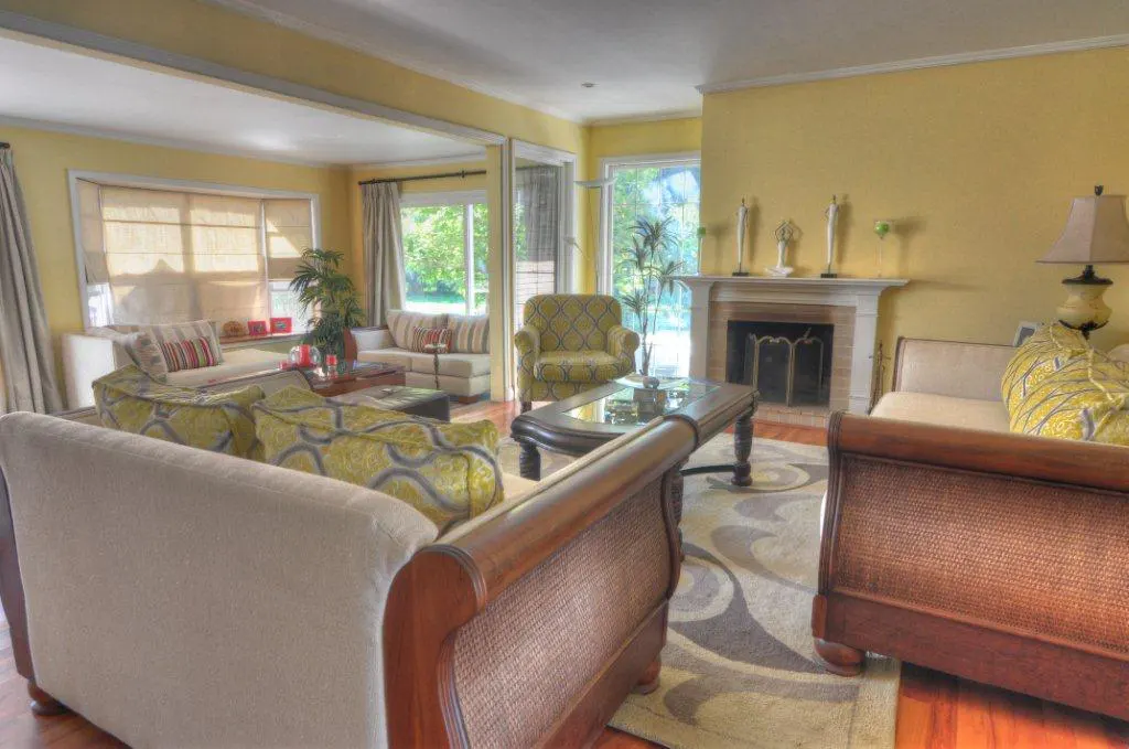 Living room with yellow walls, sofas, and a fireplace. A patterned rug covers the hardwood floor. Natural light streams through the windows.