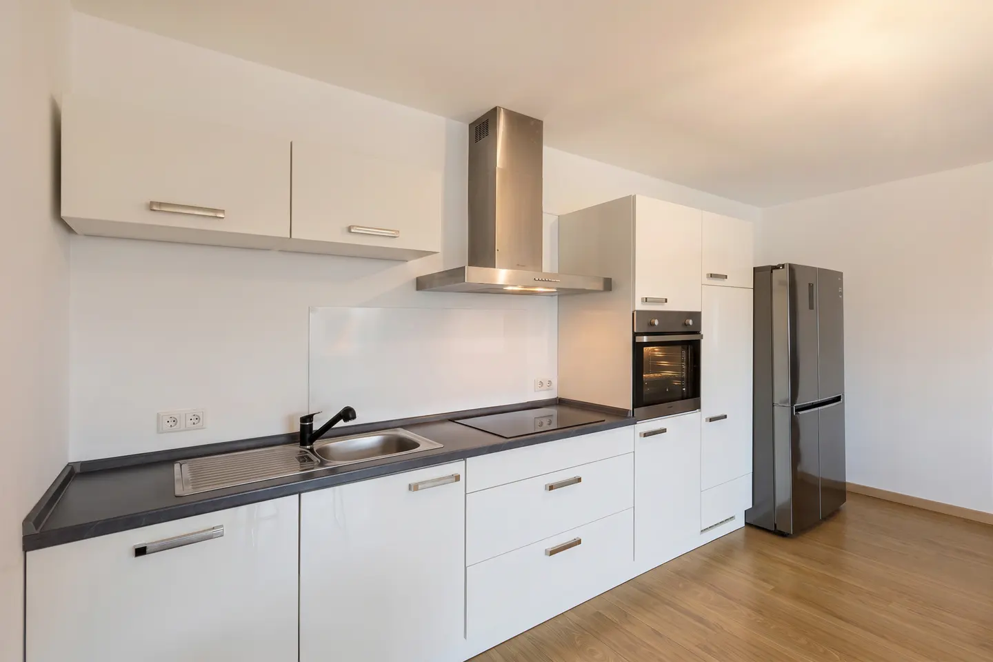 Bright kitchen with white cabinets, stainless steel appliances, dark countertops, and wood floors.