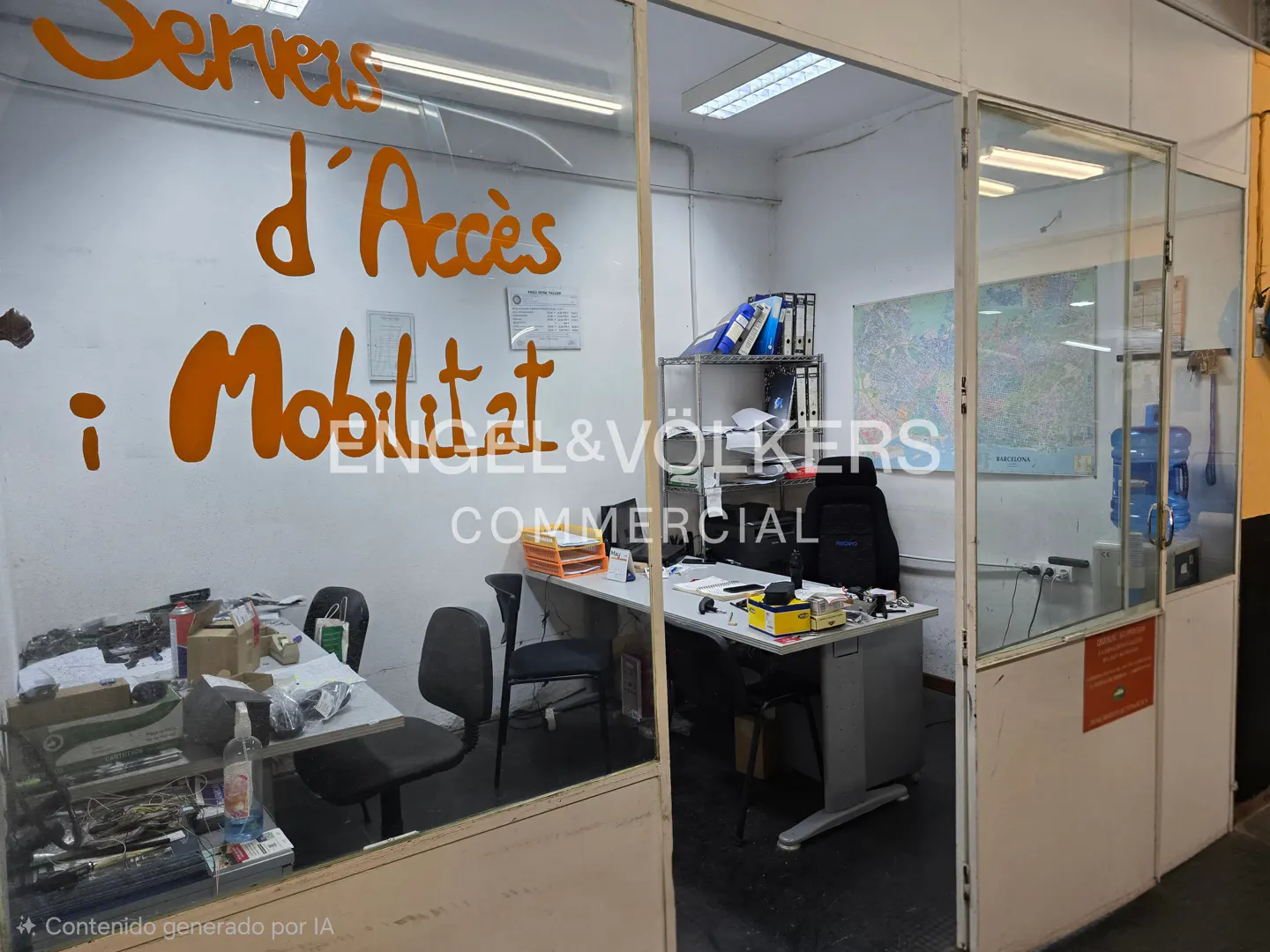 Small office seen through a glass partition with orange text reading "Serveis d'Accès i Mobilitat" on the window.