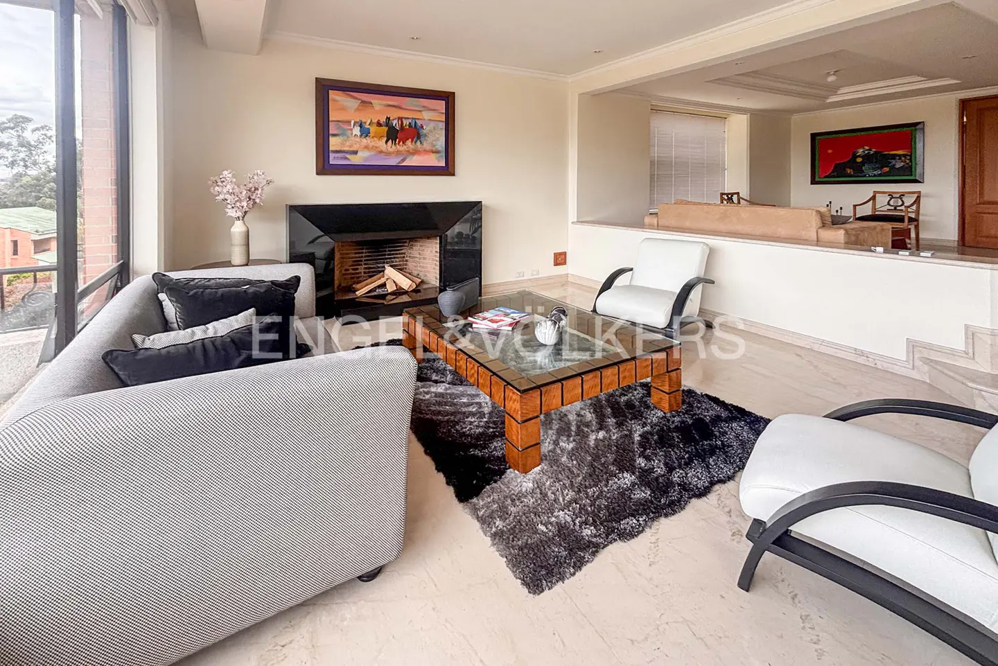Modern living room with a grey sofa, glass coffee table, black fireplace, and white armchairs on a textured rug.