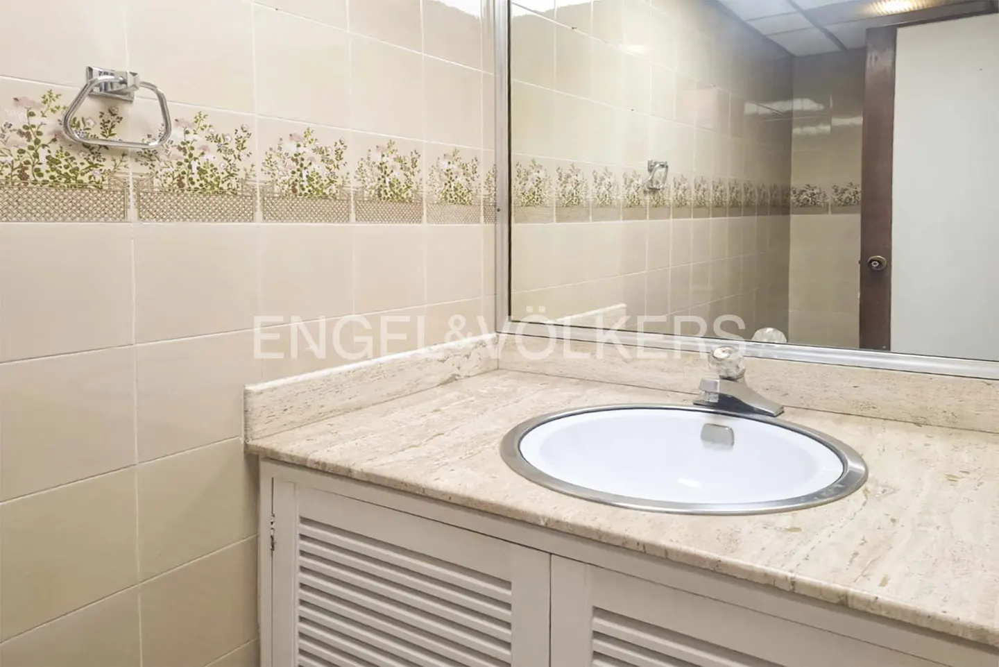 Bathroom vanity with a white circular sink, beige marble countertop, and tiled walls featuring a floral border.
