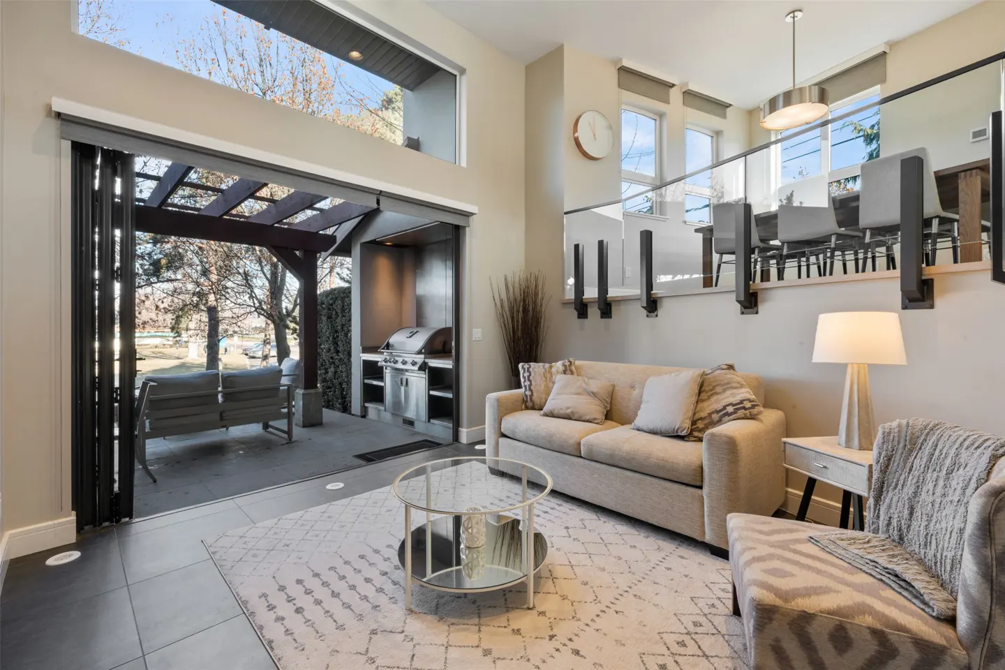 Living room with a beige sofa, patterned rug, and open doors to an outdoor patio with a grill and seating area.