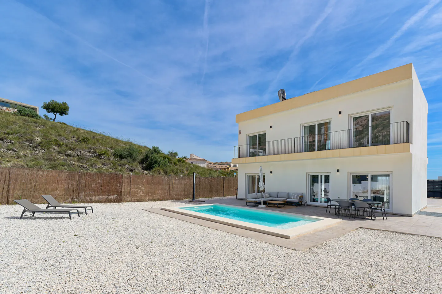 Two-story white house with a pool, lounge chairs, and outdoor seating on a sunny day.
