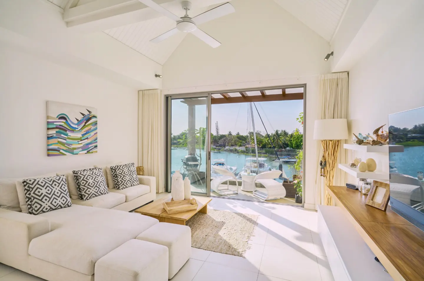 Bright living room with white sectional sofa, geometric pillows, and a wooden coffee table. Sliding glass doors open to a patio with marina views.