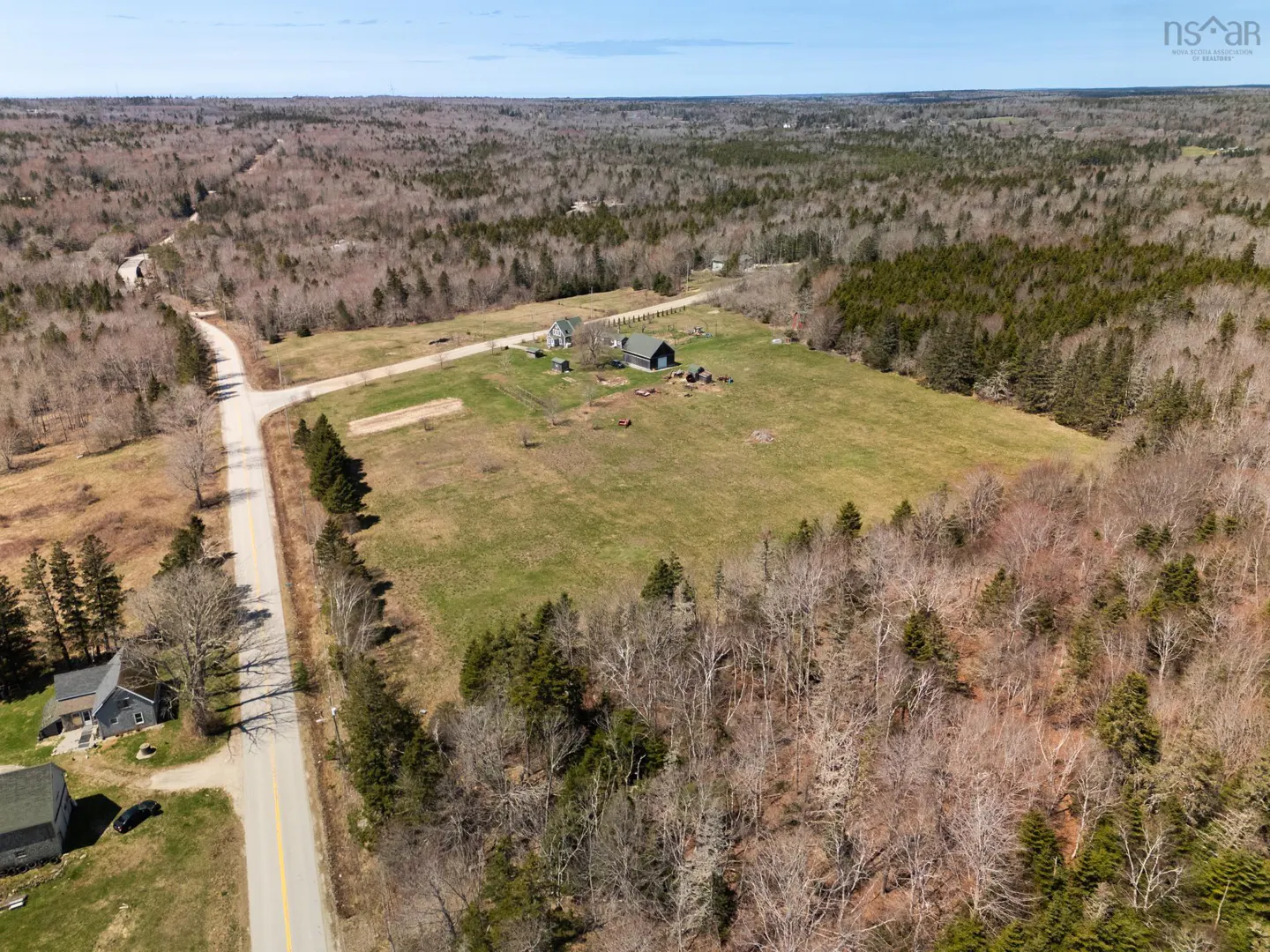 Aerial view of a rural property with a house, barn, and large green field surrounded by trees and a road.