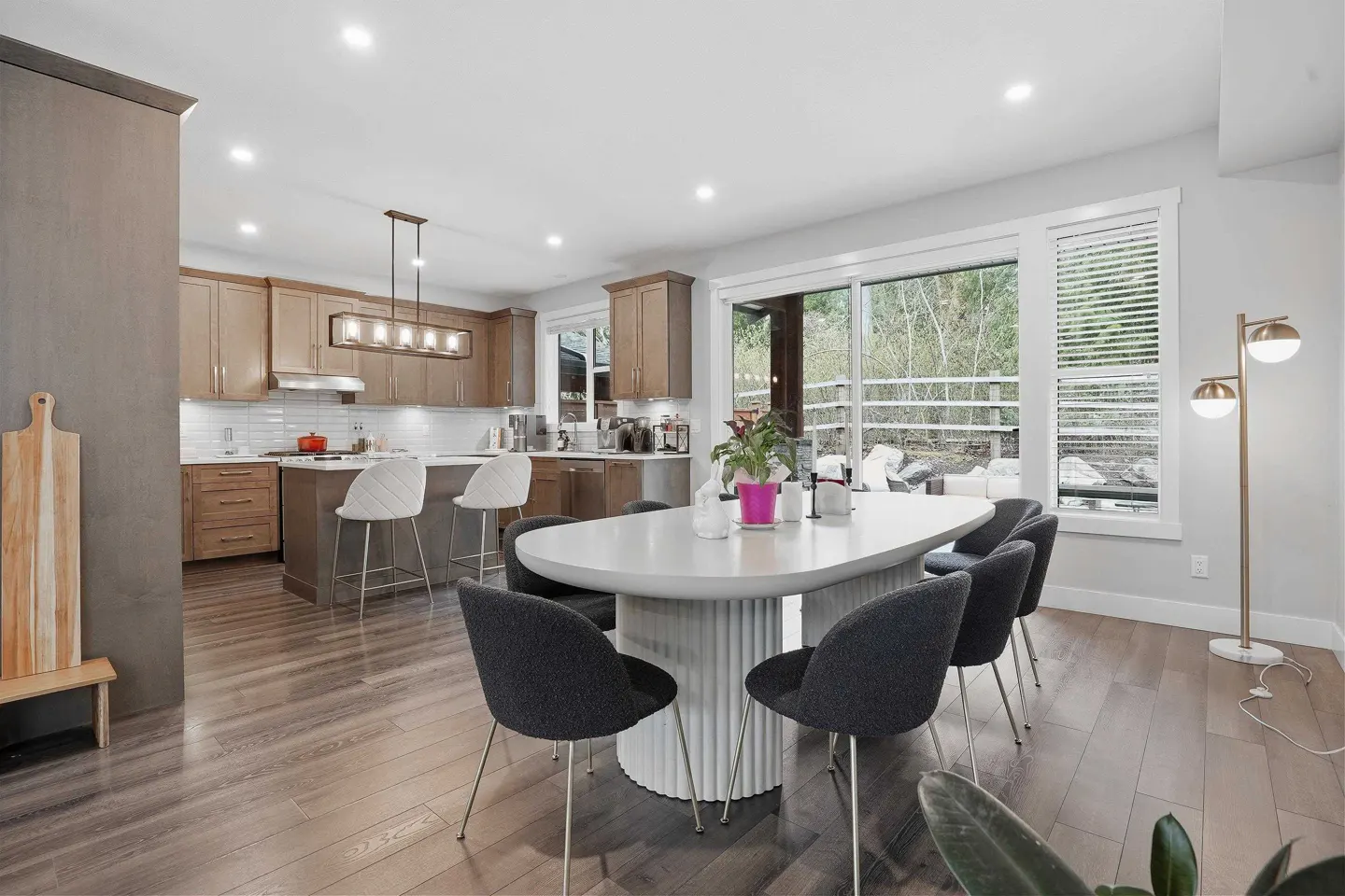 Bright, open-concept kitchen and dining area with wood floors. A white table with gray chairs sits near a large window. Kitchen island with bar stools visible.