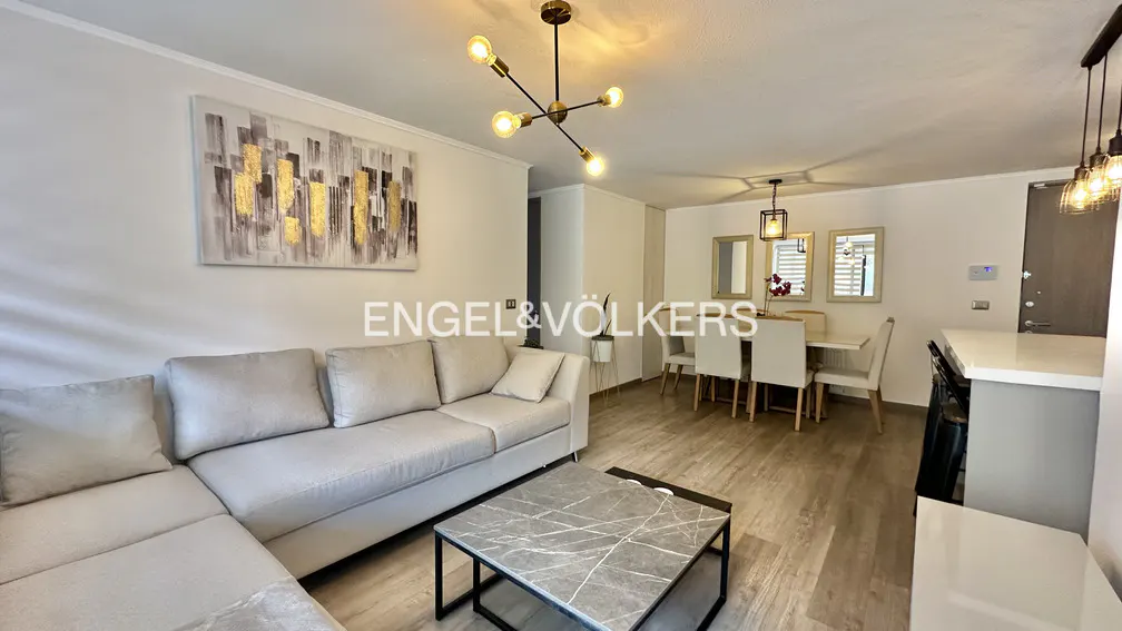 A bright, modern living space with a gray sectional sofa, marble coffee table, and dining area with white table and chairs.