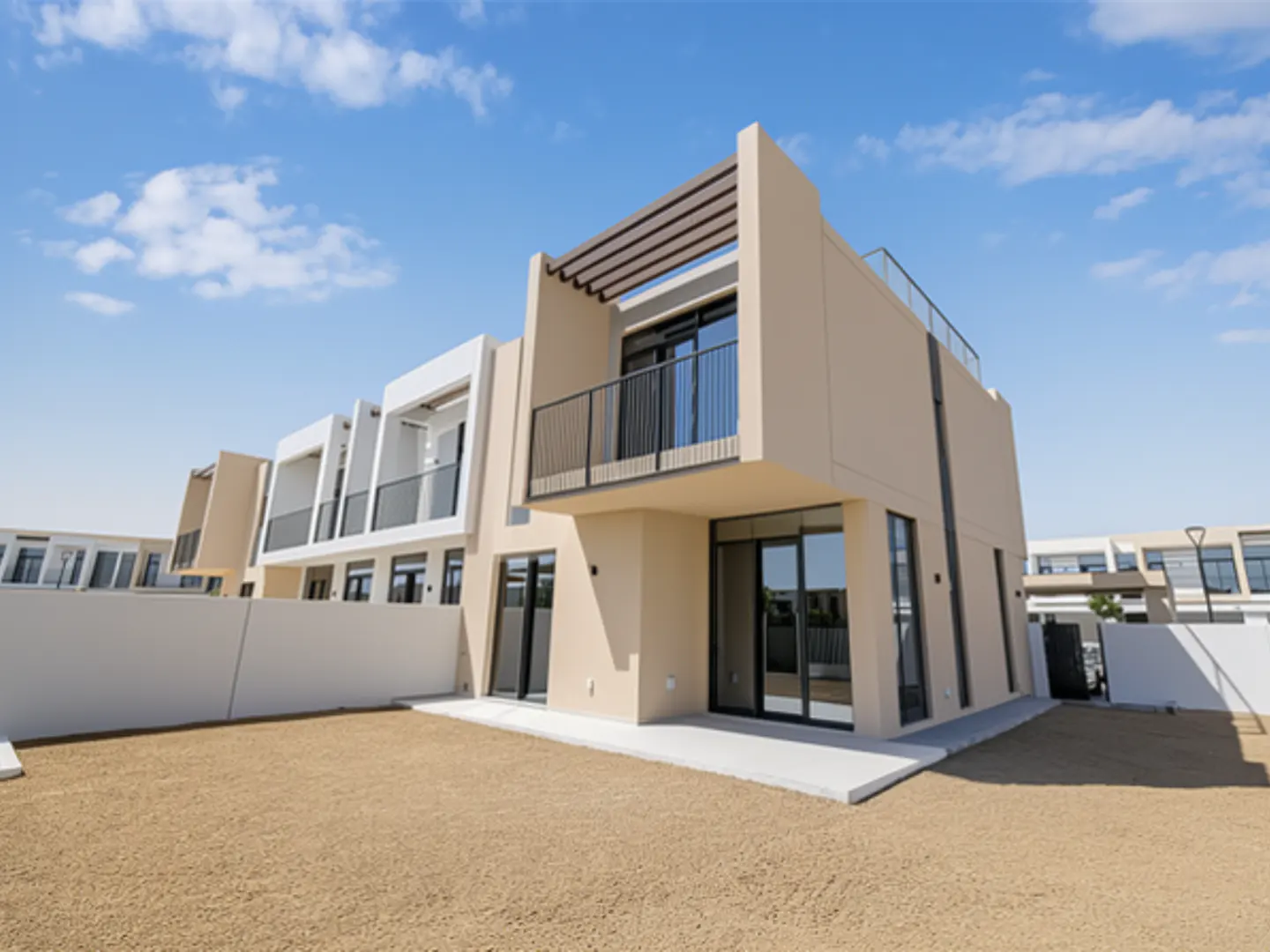 Exterior view of a modern, two-story beige townhouse with a balcony and large windows, set against a blue sky with scattered clouds.