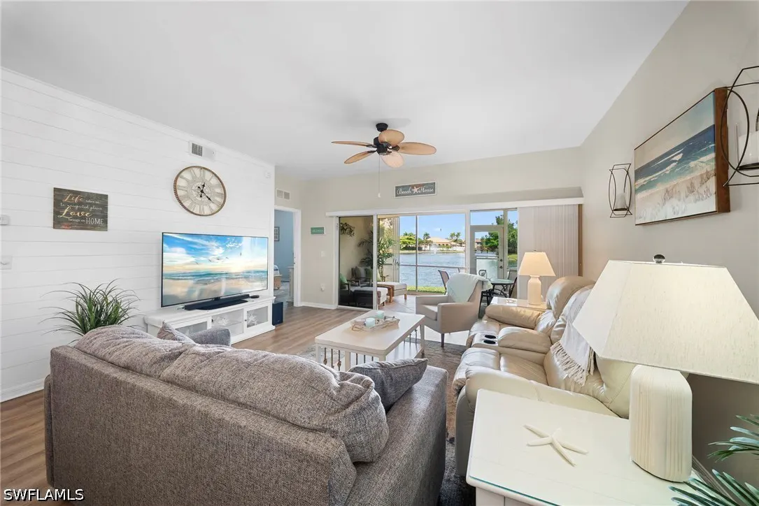 Living room with gray sofa, white walls, and a view of a lake through sliding glass doors. A TV displays a beach scene.