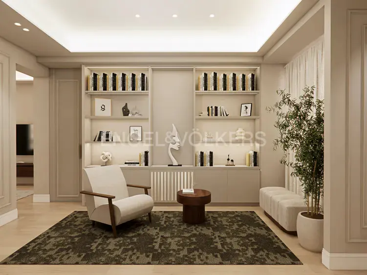 Modern beige living room with built-in bookshelves, a cream armchair, a small round table, and a potted plant on a rug.