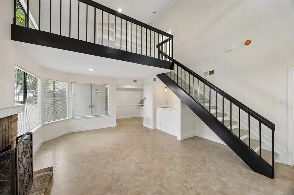 Bright living room with black staircase leading to a loft. Large windows, tile floor, and a fireplace are visible.