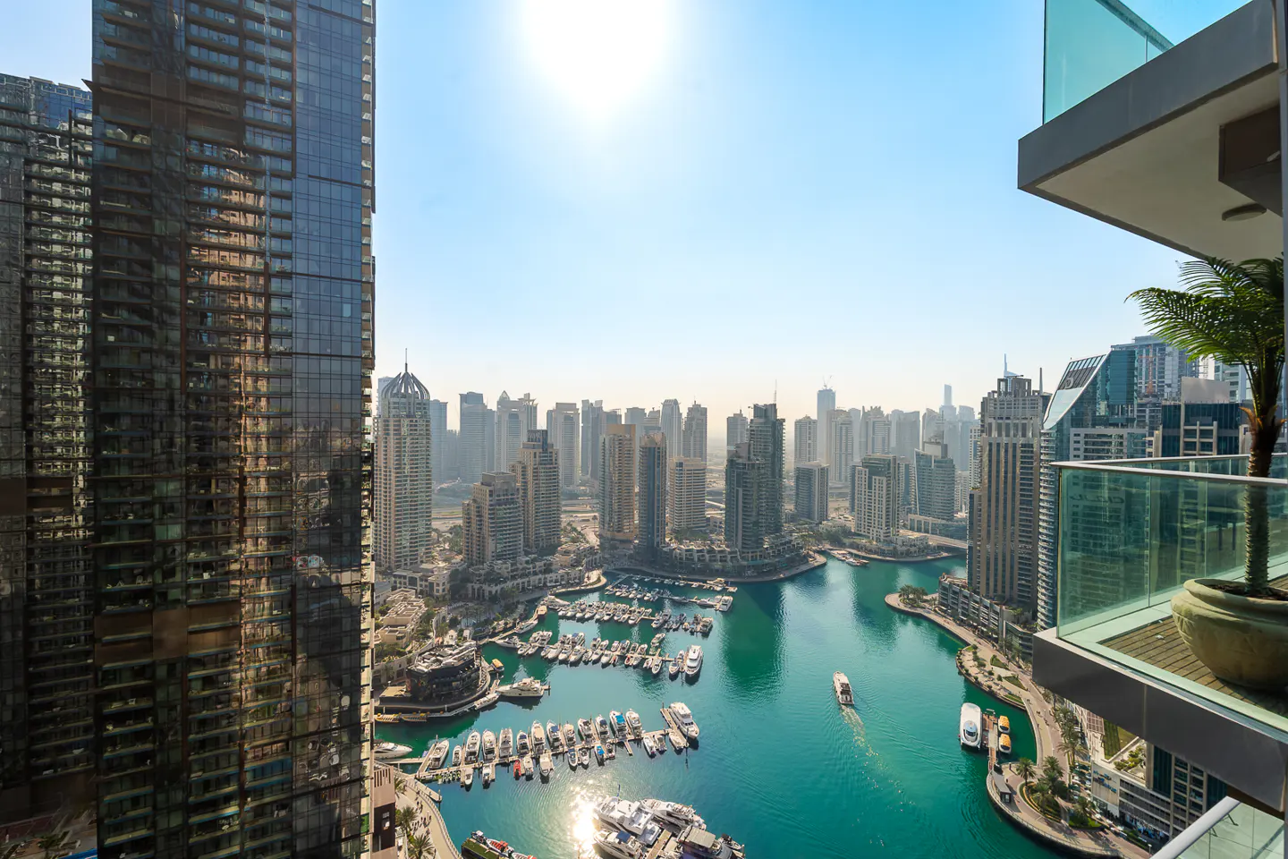 View from a high-rise balcony overlooking Dubai Marina, with turquoise water, yachts, and skyscrapers under a clear blue sky.