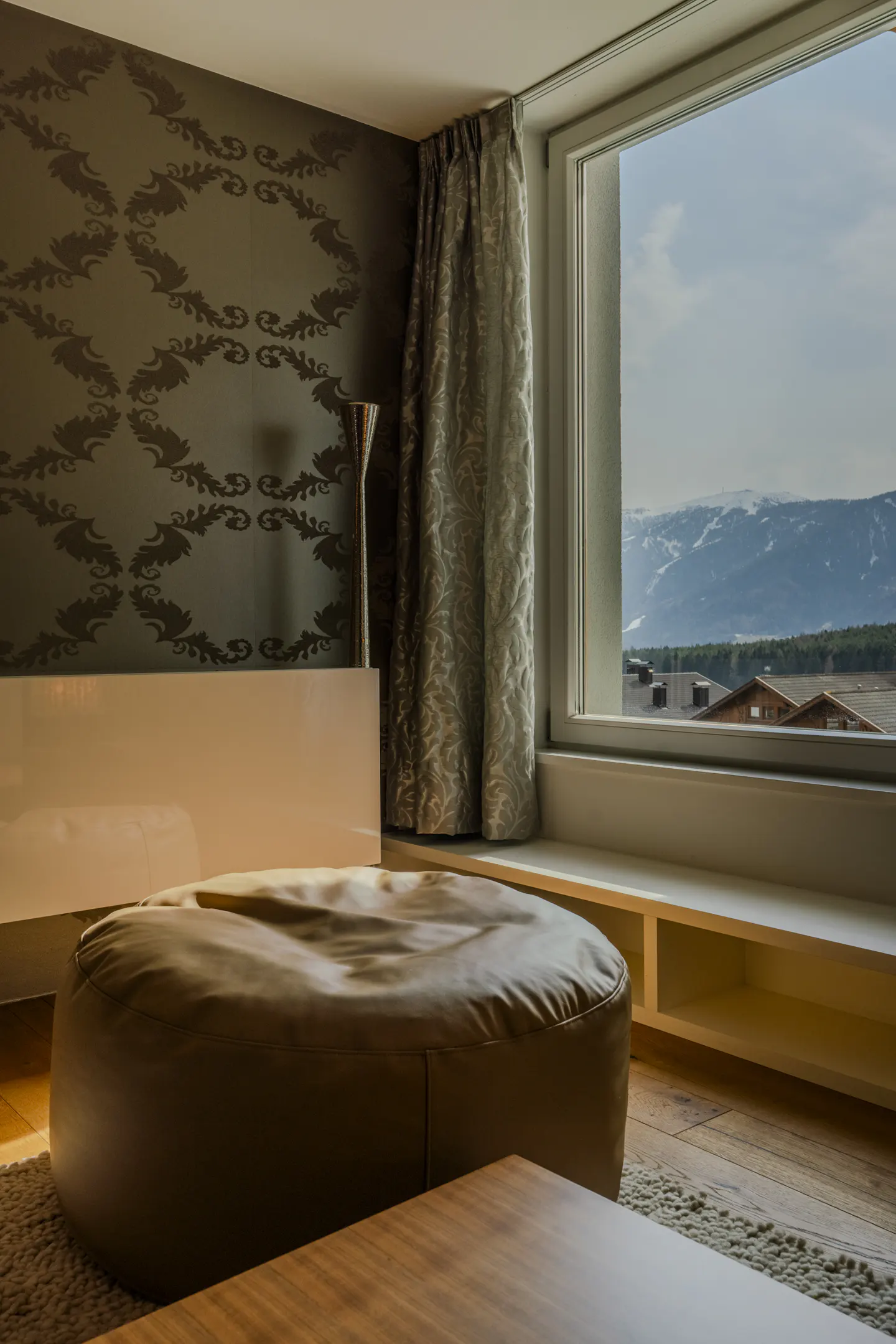 Bedroom with a brown ottoman, a white headboard, and a large window with a mountain view.