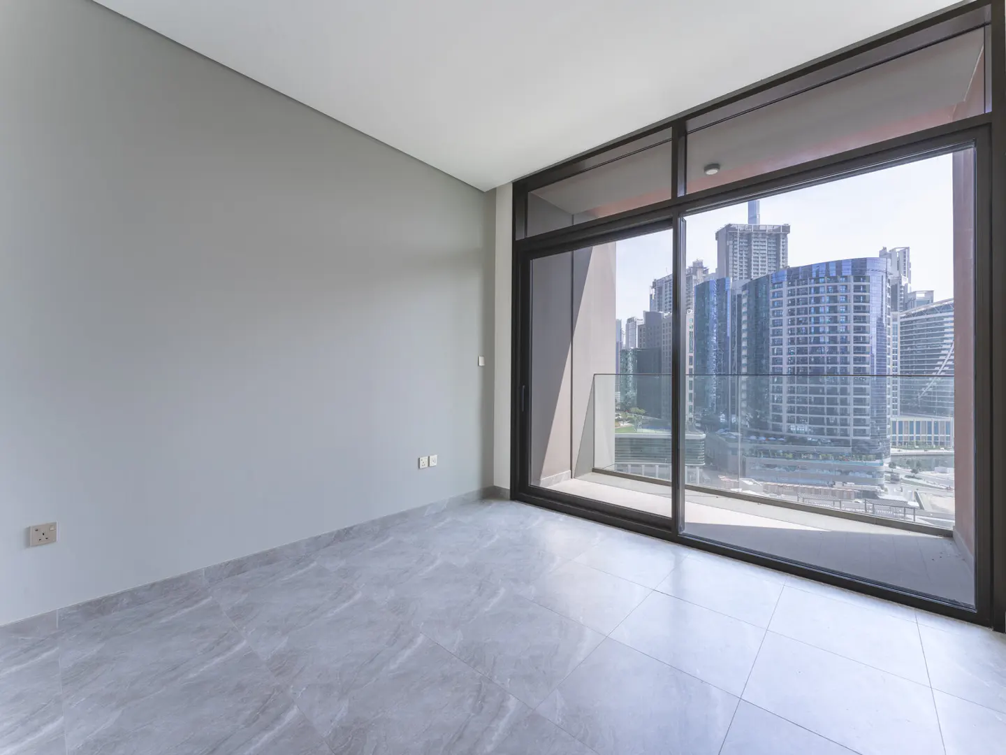 Empty room with gray walls and tile floor. Large sliding glass doors open to a balcony with a city view.