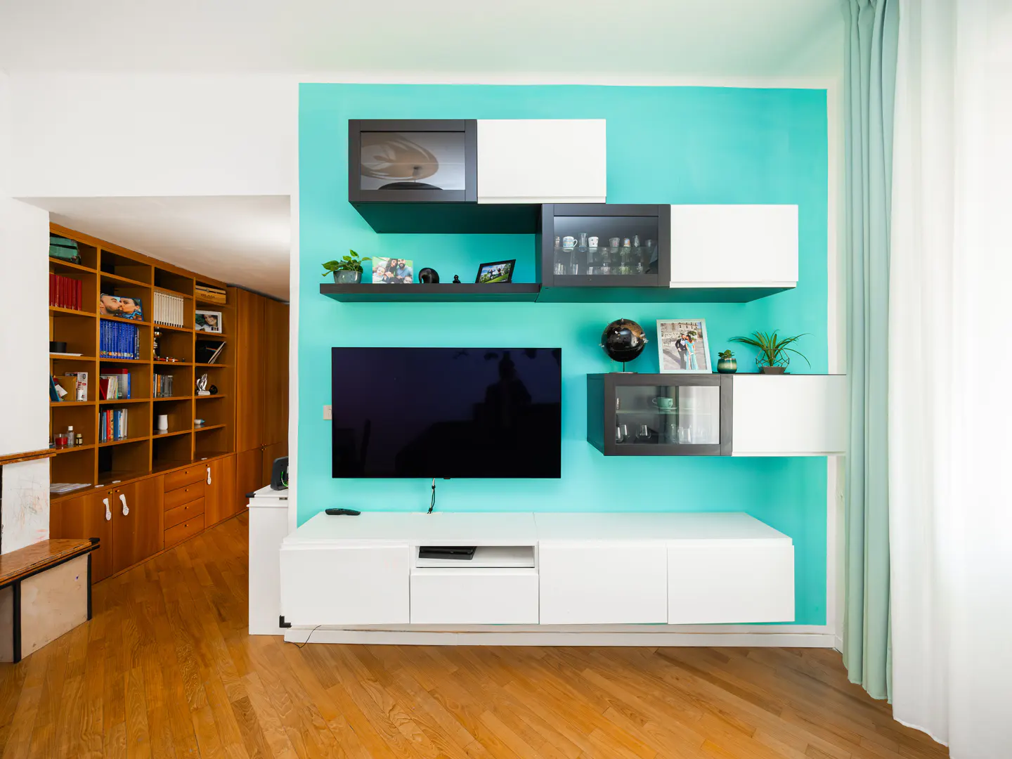 Living room with wood floors, a blue accent wall, and a white media center with a TV and floating shelves.