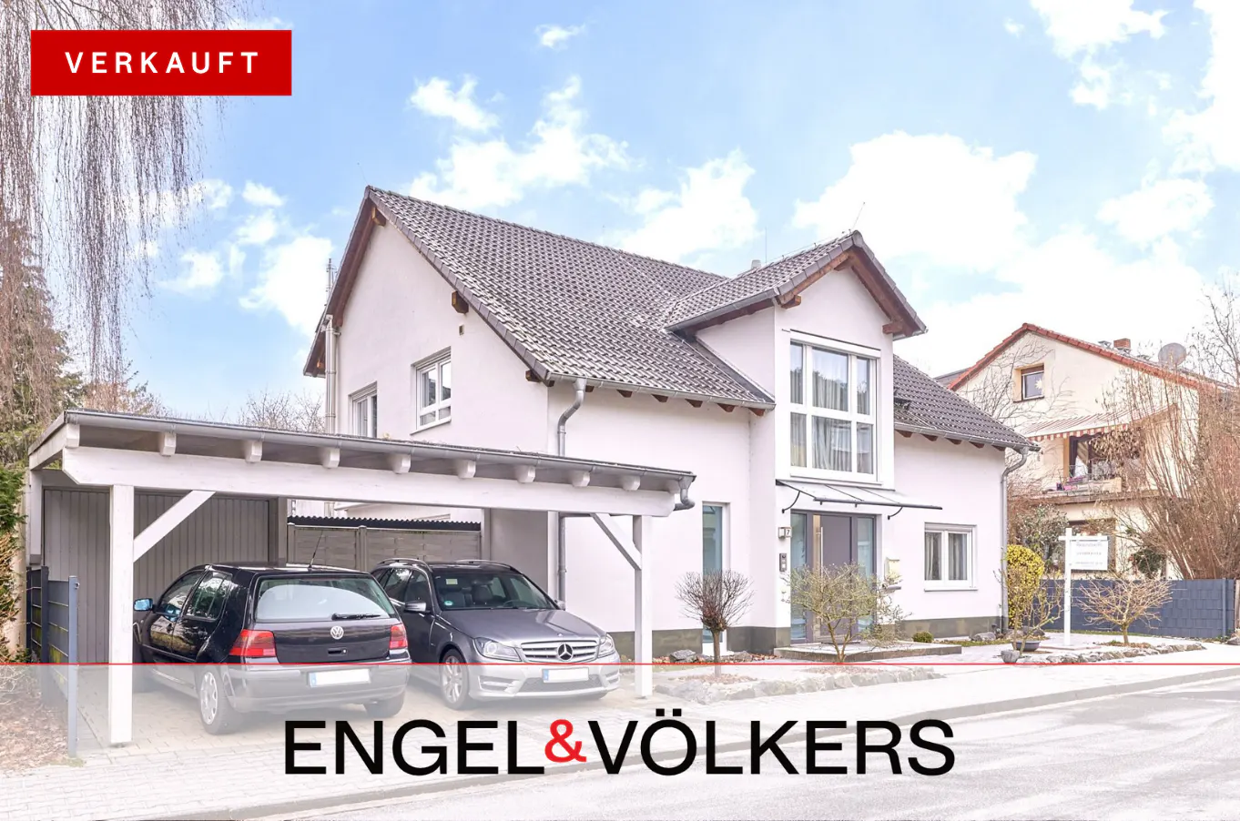 Two-story white house with a carport and two cars parked underneath. "VERKAUFT" red banner in the upper left corner.