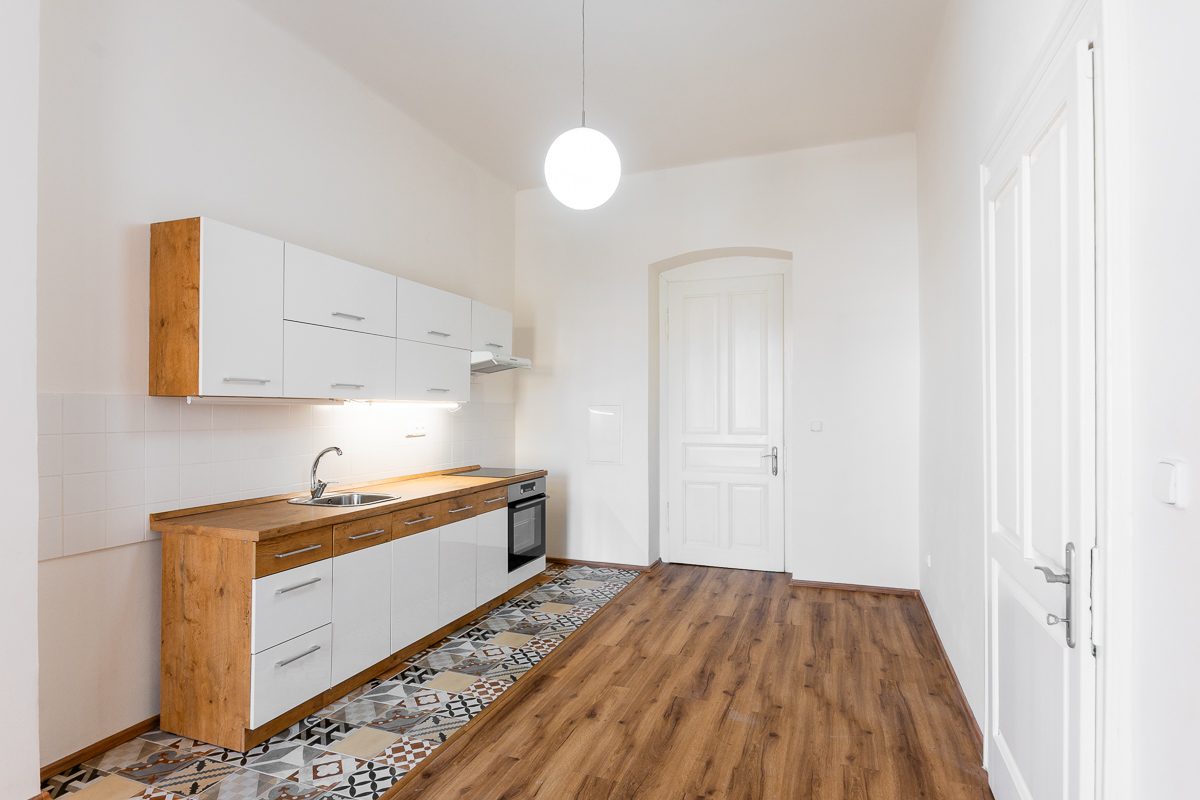 Bright, empty kitchen with white cabinets, wood countertops, and patterned tile floor. A white door is visible in the background.