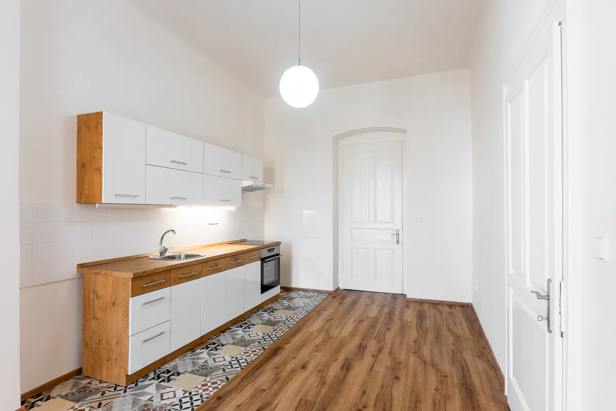 Bright, empty kitchen with white cabinets, wood countertops, and patterned tile floor. A white door is visible in the background.