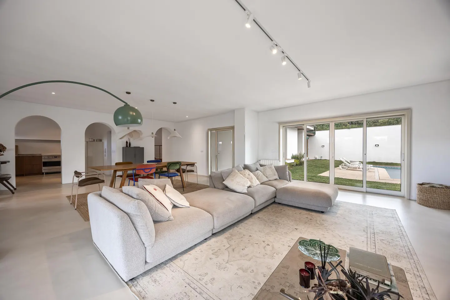 Bright, modern living room with a large gray sectional sofa, dining table with colorful chairs, and sliding glass doors to a pool area.