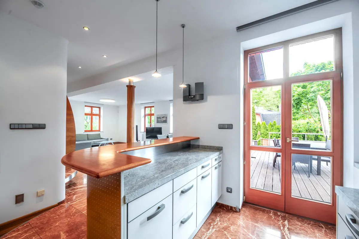 Modern kitchen with a copper-topped breakfast bar, white cabinets, and red marble floors leading to a patio door.
