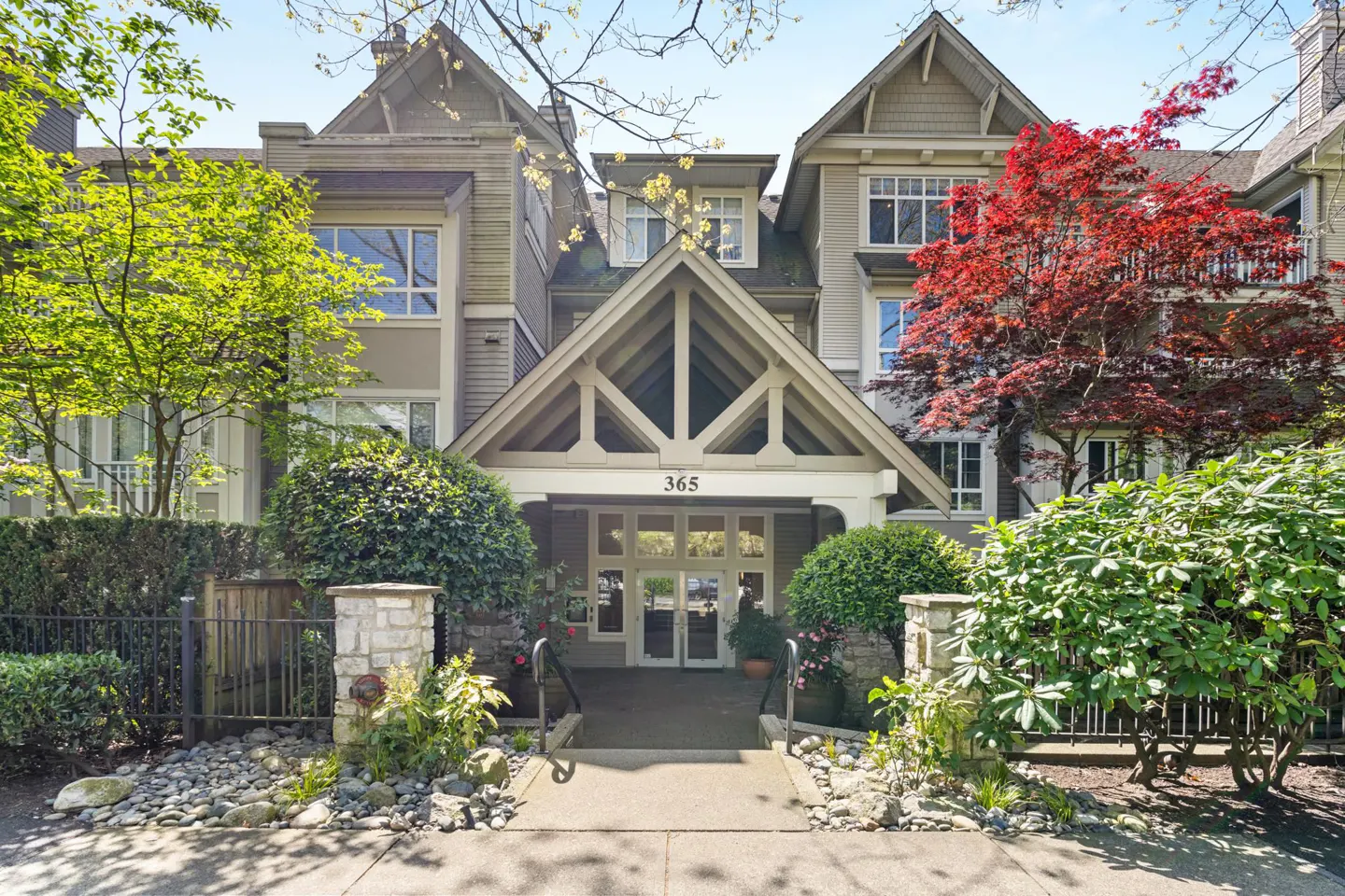 Exterior of a three-story condo building with a peaked entrance, number 365, and landscaping.