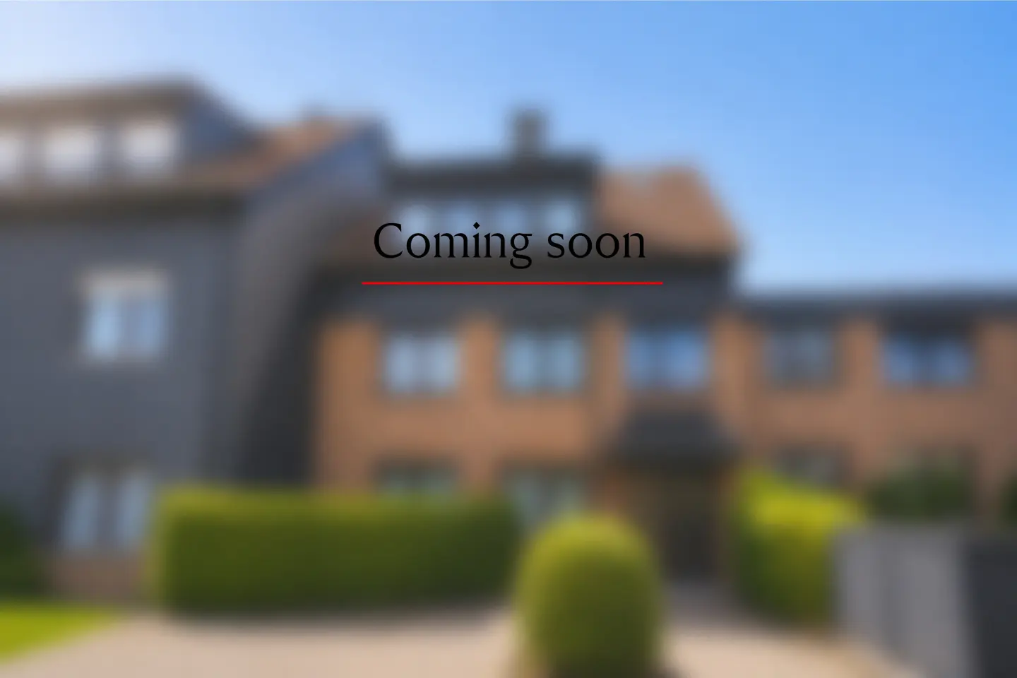 Blurred image of a modern brick house with a green hedge in front and the text "Coming soon" overlaid in the center.