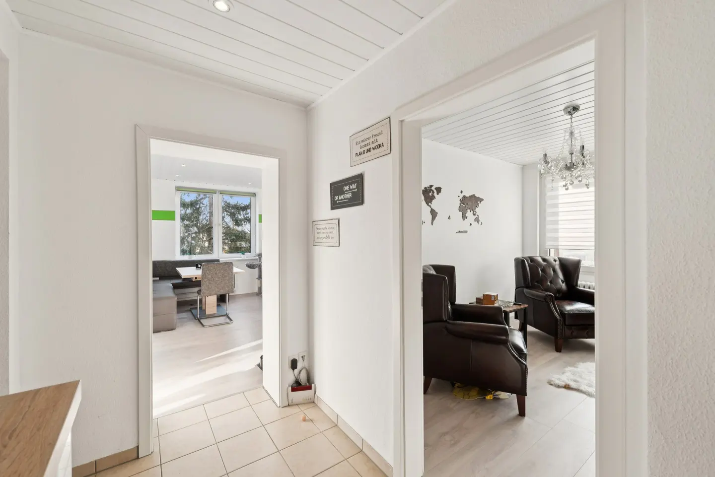 Hallway view into two rooms. One with a dining table, and the other with two brown leather armchairs and a world map on the wall.