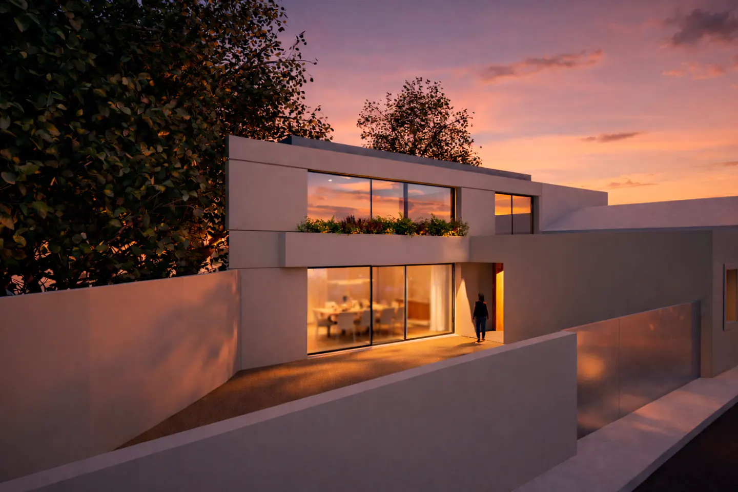 Modern white house at sunset. Person walks toward the entrance. Large windows reflect the colorful sky. Trees frame the building.