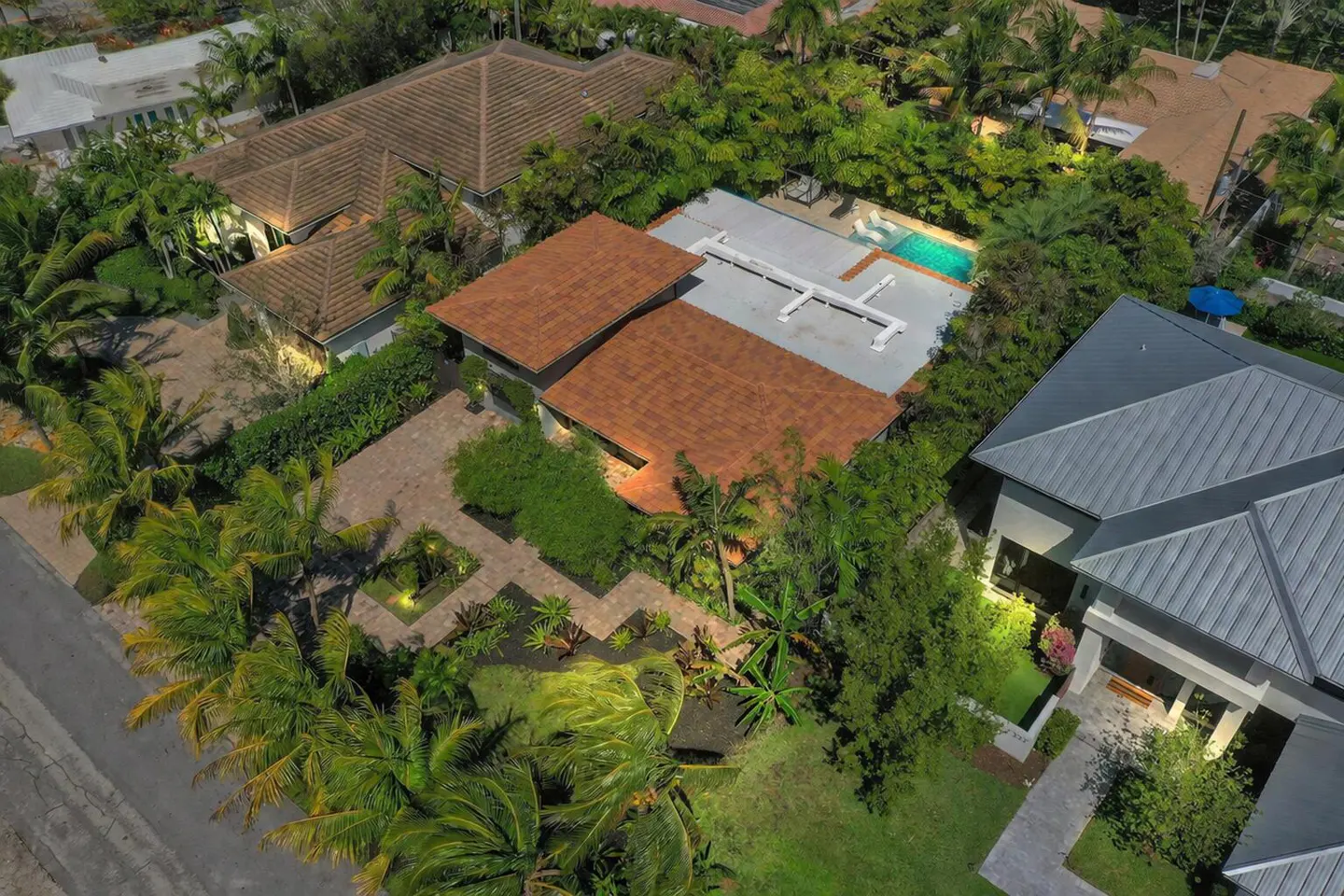 Aerial view of luxury homes with lush landscaping, brown and gray roofs, and a turquoise pool.