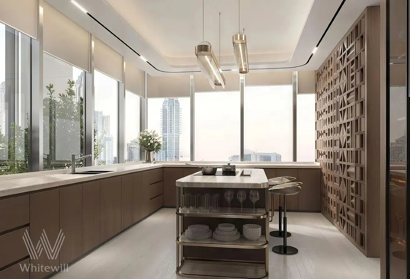 A modern kitchen with brown cabinets, a marble island, and floor-to-ceiling windows overlooking a city skyline. Two pendant lights hang above the island.