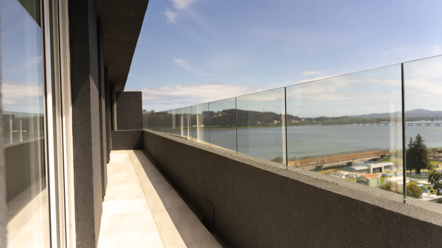 Balcony view with glass railing overlooking a river, bridge, and blue sky.