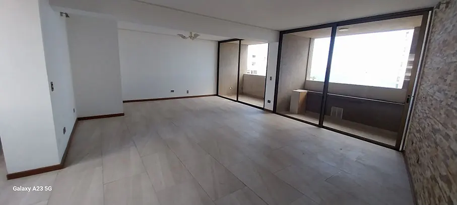Empty living room with light wood floors, white walls, and a balcony with sliding glass doors.