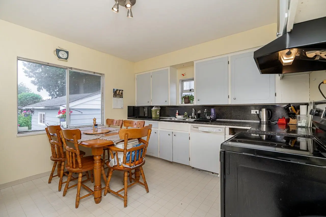Kitchen with light blue cabinets, black countertops, a black stove, and a wooden dining table with four chairs by a window.