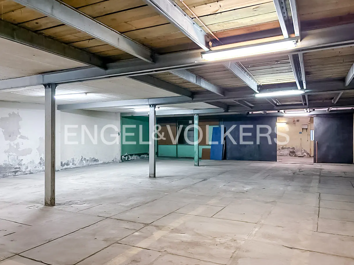 A large, empty warehouse space with concrete floors and a wooden ceiling supported by steel beams. The walls are partially painted.