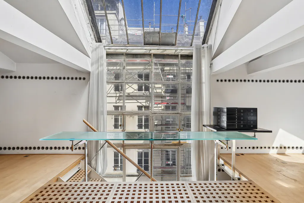 Bright room with a glass table, wood floors, and a large window showing a building with scaffolding. White walls with rows of black circles.