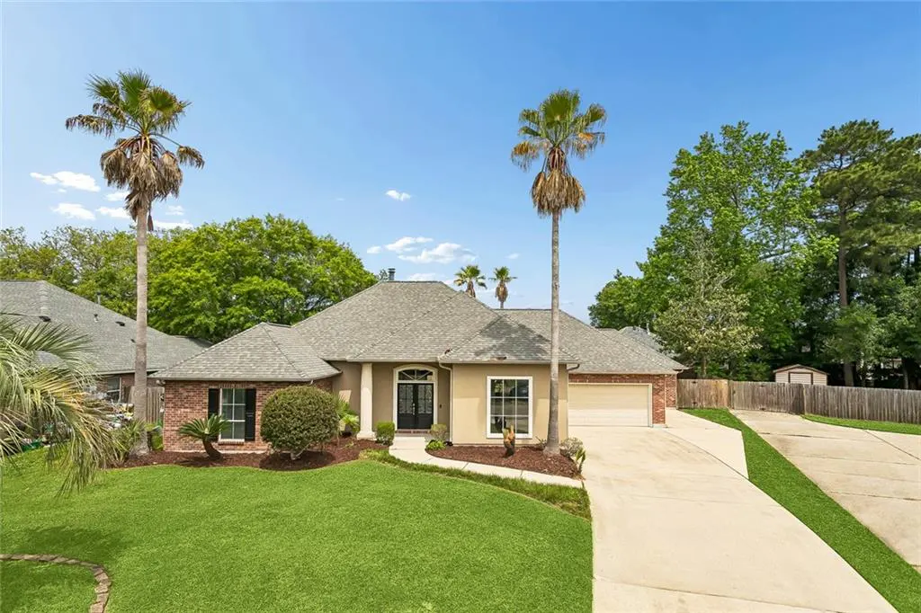 Beige single-story house with a gray roof, brick accents, and a green lawn under a blue sky with palm trees.