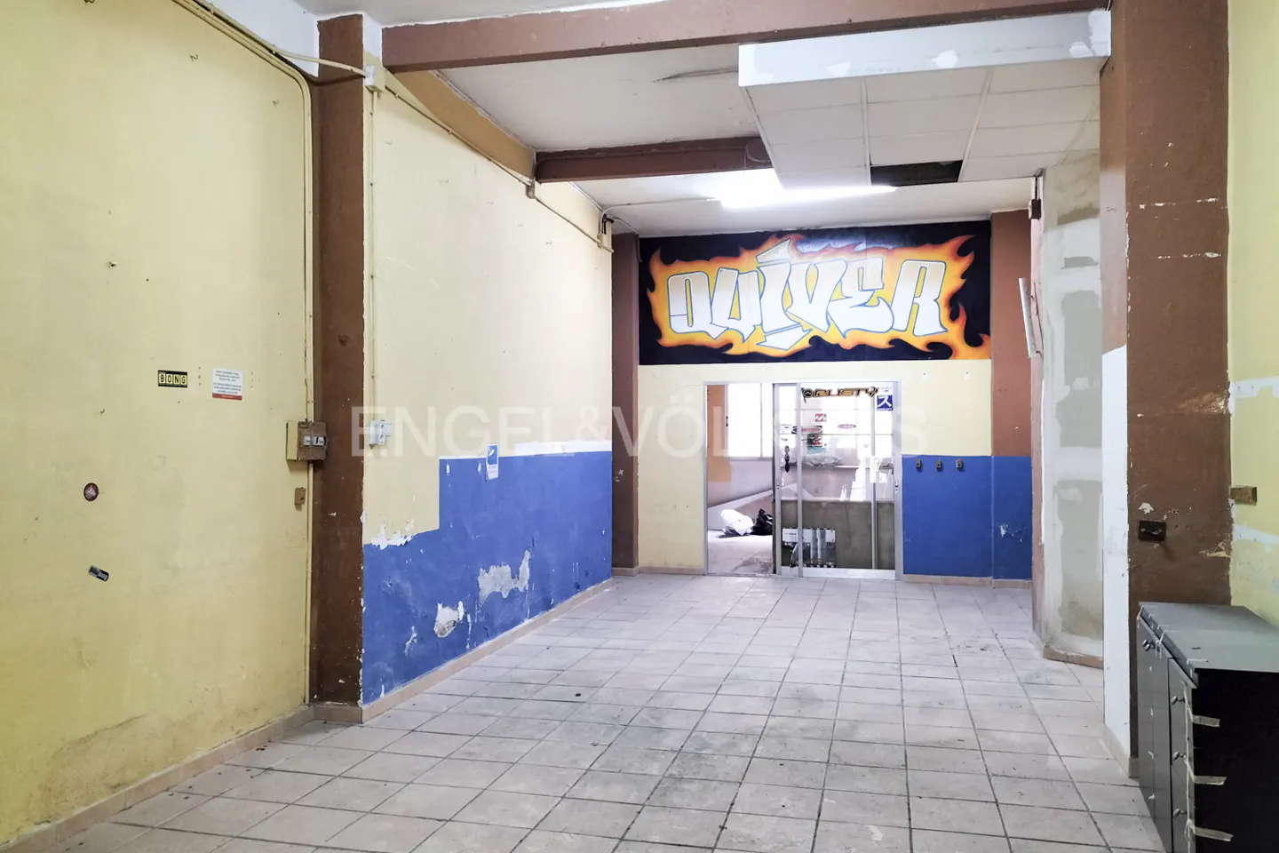 Interior of a commercial space with yellow and blue walls, tiled floor, and graffiti above a doorway.