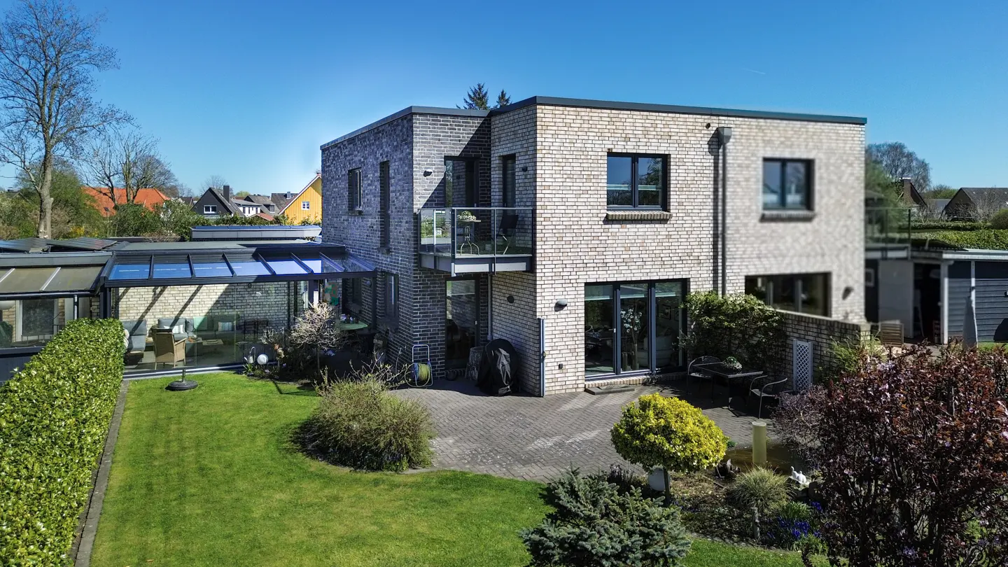 Two-story brick house with a glass-enclosed sunroom, a small balcony, and a green lawn.