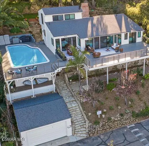 Aerial view of a white two-story house with a pool, deck, and stone staircase on a hillside.