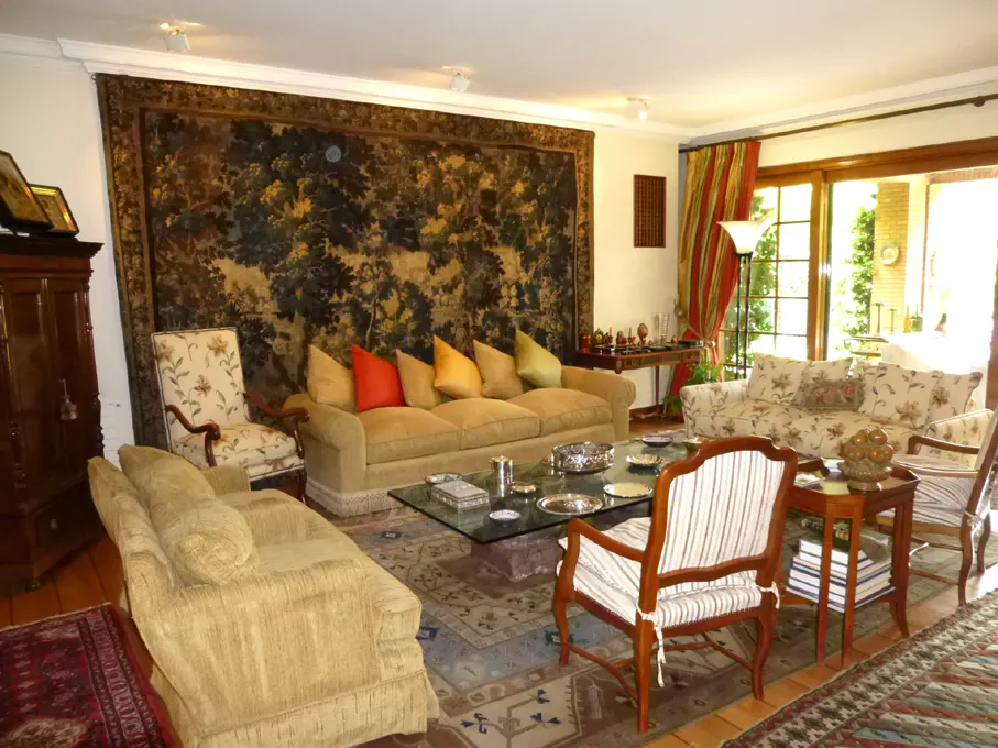 A living room with a large tapestry on the wall, a tan sofa with colorful pillows, and a glass coffee table.