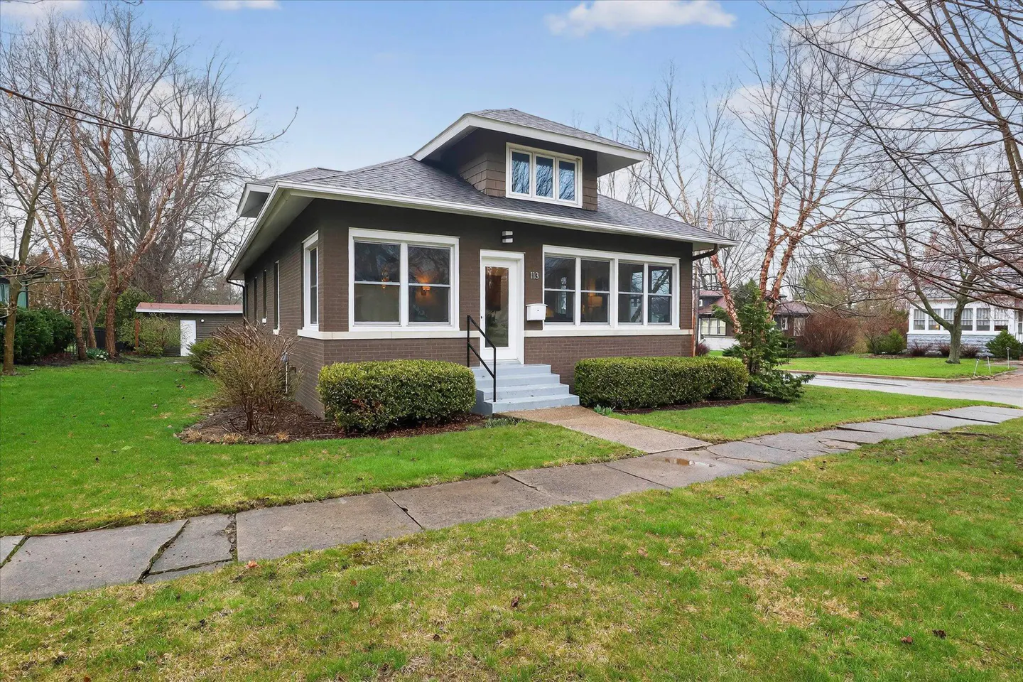 Two-story brown house with white trim, gray roof, and green lawn on a sunny day.