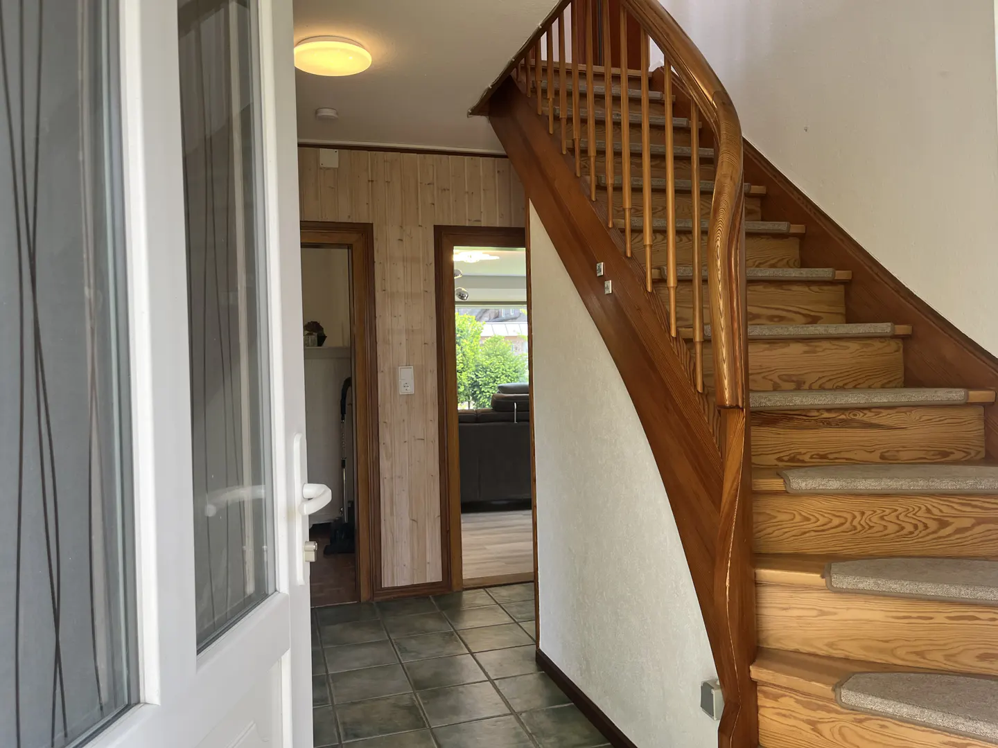 Entryway with tiled floor, wooden staircase with carpet treads, and doorways leading to other rooms.