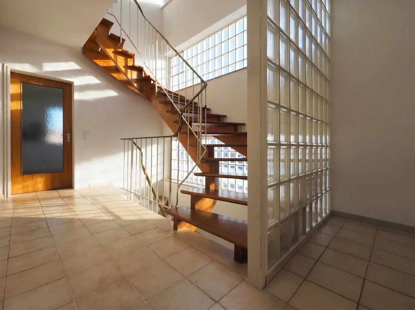 Interior view of a home featuring a wooden staircase with white railings, a glass block wall, and a wooden door.
