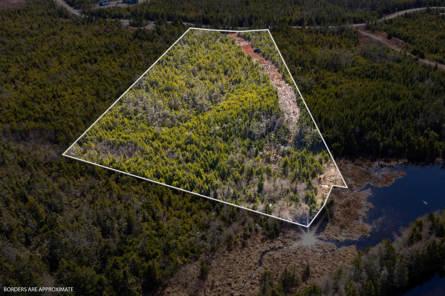 Aerial view of a wooded property outlined in white, adjacent to a dark blue lake. The land includes green trees and a clearing.