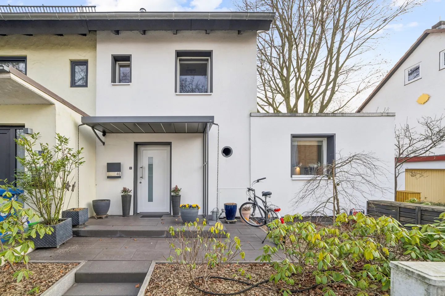 Exterior view of a modern two-story white house with gray trim, a front door, and a bicycle parked outside.