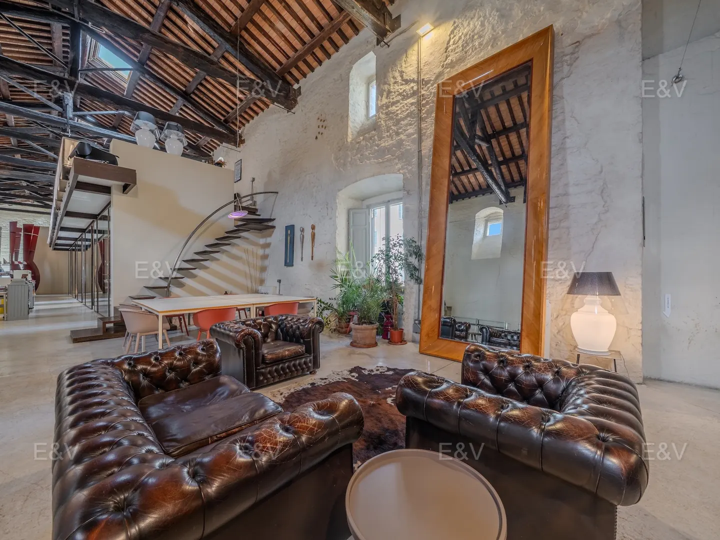 Living room with brown leather sofas, cowhide rug, and large mirror in a converted warehouse with exposed beams.