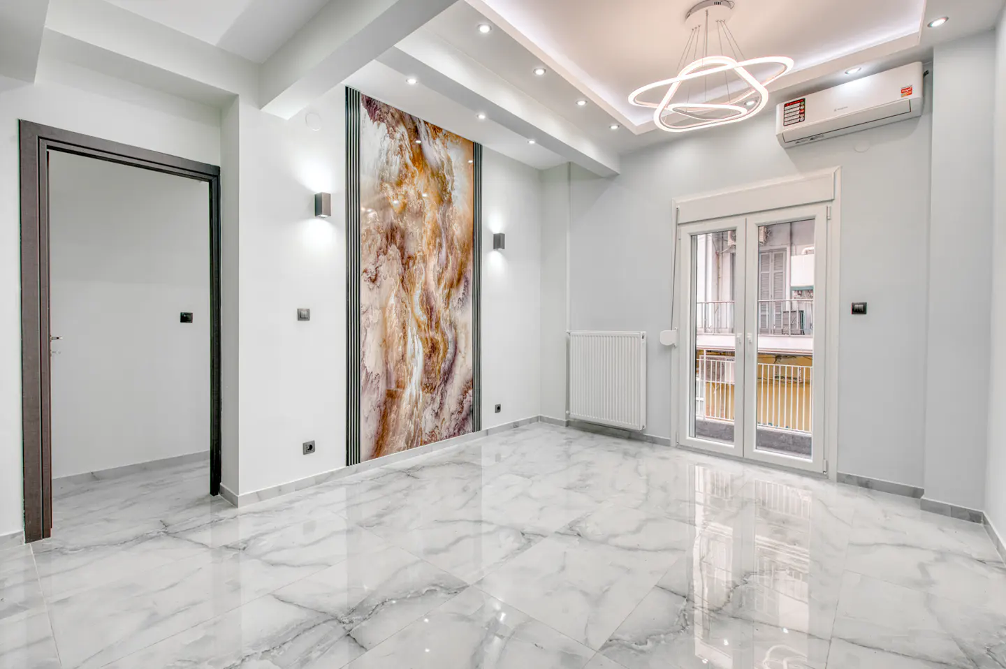 Bright, empty room with marble floors, white walls, and a decorative marble panel. A modern light fixture hangs from the ceiling.