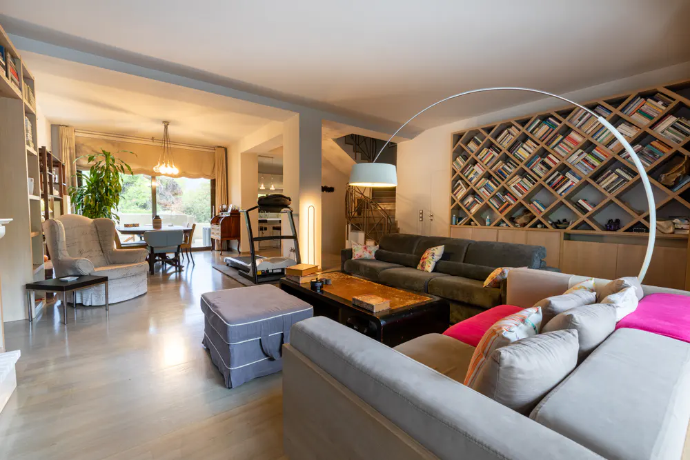 Open-concept living room with hardwood floors, gray sofas, a bookshelf wall, and a dining area visible in the background.