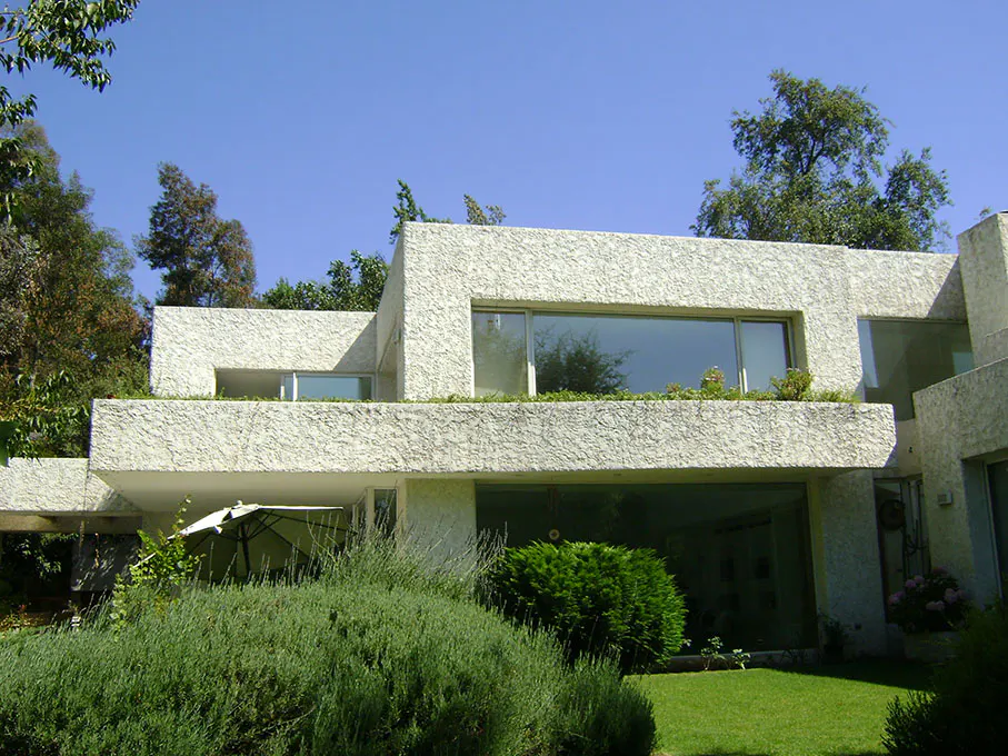 Modern white stucco house with large windows, green lawn, and trees under a clear blue sky.